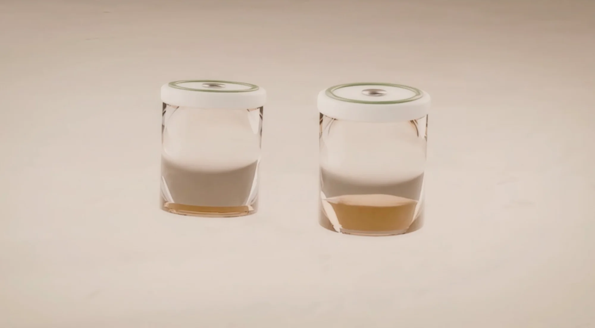 Two clear glass scent pods with linen caps and grass-green bands, each holding golden oil.